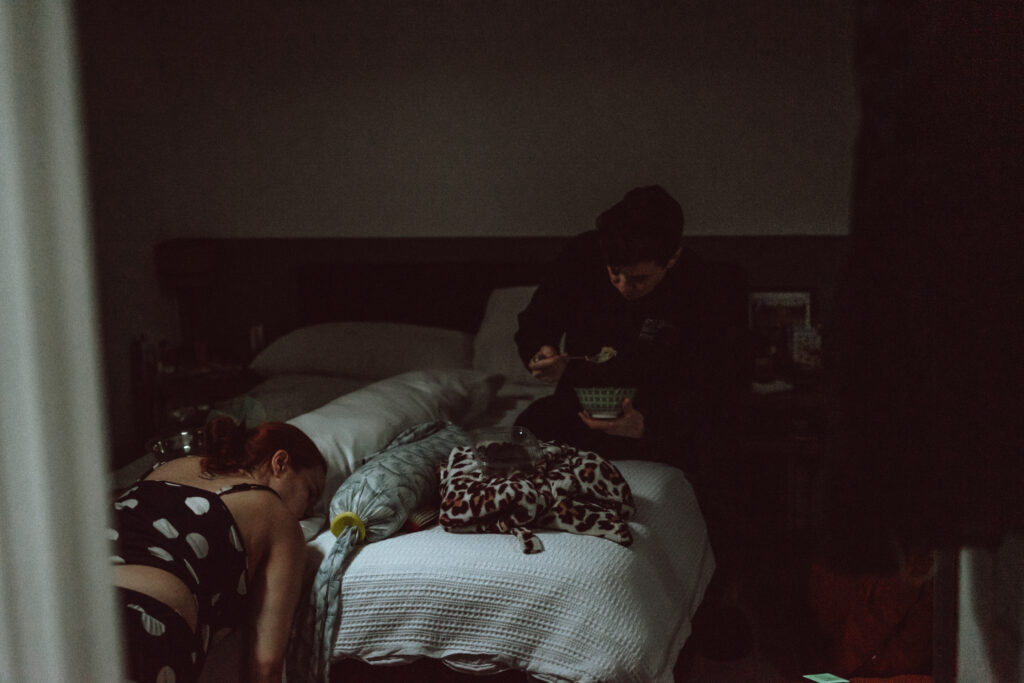 QEQM St Peters Midwife-Led Unit Birth. Margate birth with doula care in woman's home showing birth partner on bed eating breakfast before transferring to QEQM