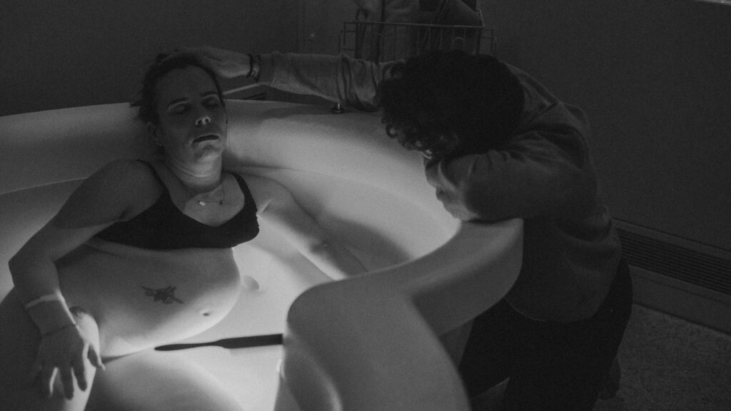 QEQM St Peters Midwife Led Unit Birth Pool with Margate Doula Support and Birth photographer Naomi Gale. Showing woman in birth pool with partner tending to her forehead.