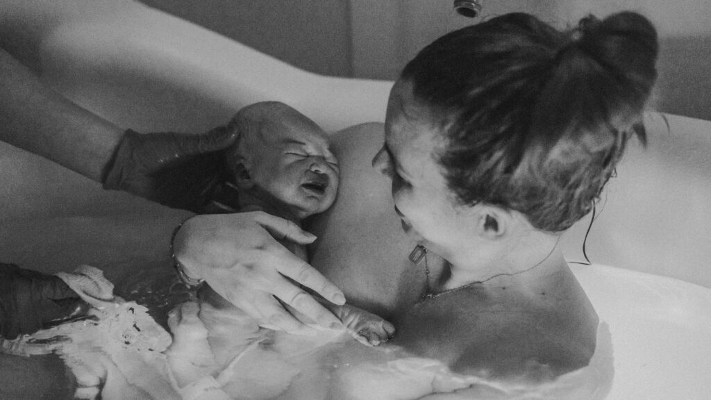 QEQM St Peters Midwife Led Unit Birth Pool with Margate Doula Support and Birth photographer Naomi Gale. Showing woman in birth pool with her baby being passed to her by a midwife
