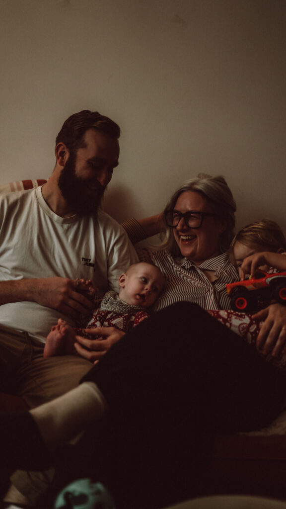 Margate family portrait shoot with family laughing on the sofa with a toddler and a new baby
